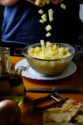 Küchenchefin filtert frische rohe Kartoffelstücke mit Sieb über weißem Teller in der Küche — Stockfoto