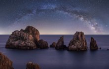 Große raue Klippen auf blauem, ruhigem Ozean am hellen Abend unter farbenfrohem Sternenhimmel mit Milchstraße — Stockfoto