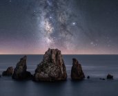 Big rough cliffs on blue calm ocean during bright evening under colorful starry sky with milky way — Stock Photo