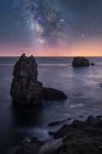 Большой грубый скалы на голубом спокойном океане в течение яркого вечера под красочным звездным небом с молочным путем — стоковое фото