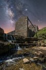From below of ancient stone castle and small waterfall on stairs under dark sky with stars and milky way — Stock Photo