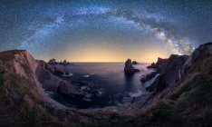 Grandes acantilados ásperos en el océano azul tranquilo durante la noche brillante bajo el cielo estrellado colorido con la vía láctea - foto de stock