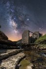 Знизу стародавнього кам'яного замку і невеликого водоспаду на сходах під темним небом з зірками і молочним способом — стокове фото