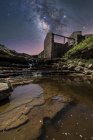 From below of ancient stone castle and small waterfall on stairs under dark sky with stars and milky way — Stock Photo