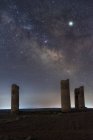 Torres de pedra antigas em solo arenoso vazio sob céu estrelado escuro com caminho leitoso — Fotografia de Stock