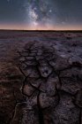 From above of dry cracked surface of ground and colorful night starry sky on horizon — Stock Photo