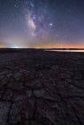 Desde arriba de la superficie seca agrietada del suelo y colorido cielo estrellado de noche en el horizonte - foto de stock
