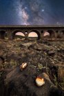 Rocky terra e vecchio ponte di pietra con cielo notturno colorato con via lattea e stelle su sfondo — Foto stock