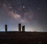 Древние каменные башни на пустой песчаной почве под темным звездным небом с млечным путем — стоковое фото