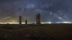 Древние каменные башни на пустой песчаной почве под темным звездным небом с млечным путем — стоковое фото