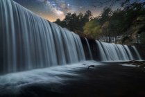 Bela cachoeira rochosa poderosa e fluxo de água com céu estrelado noite colorida no fundo — Fotografia de Stock