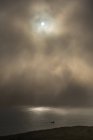 Surface calme de l'océan et falaise rugueuse sous un brouillard épais avec un soleil éclatant dans un ciel nuageux — Photo de stock