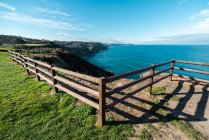 D'en haut de la clôture en bois sur le bord vert de la falaise avec un océan bleu coloré et le ciel sur le fond — Photo de stock