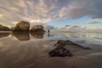 Grandi formazioni rocciose sulla spiaggia sabbiosa vuota dell'oceano con cielo serale nuvoloso e luminoso sullo sfondo — Foto stock