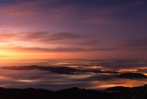 Вид з повітря на сучасне місто і гори, вкриті кліщами хмар під барвистим небом під час сходу сонця — стокове фото