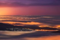 Aerial view of modern city and mountains covered with tick clouds under colorful sky during sunrise — Stock Photo