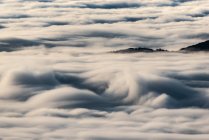 From above of black peaks of powerful mountains among soft white thick clouds — Stock Photo