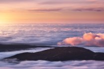 De cima de picos pretos de montanhas poderosas entre nuvens espessas brancas suaves ao nascer do sol — Fotografia de Stock