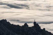 Силуэт неузнаваемого человека, занимающегося йогой в изящной позе, стоящего на вершине грубой скалы с красочными облаками на заднем плане — стоковое фото