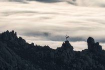 Silhueta de pessoa irreconhecível fazendo ioga em pose graciosa em pé no pico de penhasco áspero com nuvens coloridas no fundo — Fotografia de Stock