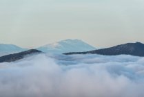 De cima de picos pretos de montanhas poderosas entre nuvens grossas brancas suaves — Fotografia de Stock
