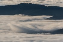 Зверху чорні вершини могутніх гір серед м'яких білих товстих хмар — стокове фото