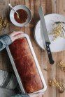 Von oben beschnittene, unkenntlich gemachte Hand mit rechteckigem Laib frischem Brioche-Brot auf Holztisch mit Schüssel mit Marmelade und Messer — Stockfoto