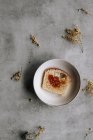 Vista dall'alto di fetta fresca di pane brioche spalmato con marmellata marrone su piatto su tavolo grigio con fiori — Foto stock