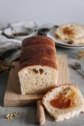 Сверху кусок вкусного булочного хлеба на столе с буханкой на деревянной доске на кухне — стоковое фото