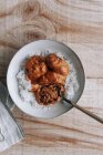 Vista dall'alto di ciotole di riso e deliziose polpette di lenticchie con salsa al curry posizionate vicino a spezie e tovaglioli sul tavolo di legno a casa — Foto stock