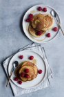 From above top view of tack of tasty pancakes with ripe raspberries placed on plate near spoons on gray background — Stock Photo