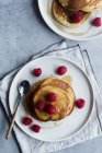 From above top view of tack of tasty pancakes with ripe raspberries placed on plate near spoons on gray background — Stock Photo