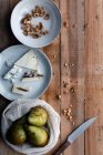 From above cotton sack with fresh pears and plate with walnuts placed near cheese and knife on timber table — Stock Photo