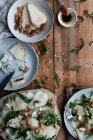 From above plates of delicious pear and walnuts salad with cheese and arugula placed on lumber table near cooking ingredients — Stock Photo