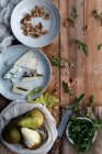 Vista dall'alto di piatti con noci e formaggio posizionati vicino al sacchetto di cotone con pere mature e ciotola con rucola fresca sul tavolo di legname durante la preparazione dell'insalata — Foto stock