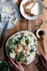 Vista dall'alto di persona anonima mettere piatto di insalata di pere con rucola sul tavolo di legno vicino formaggio e noci in cucina — Foto stock