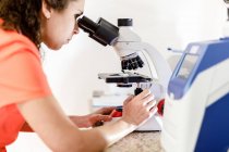 Back view of unrecognizable female doctor looking through modern microscope while at sample while working in modern clinic — Stock Photo