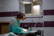 Visão lateral do veterinário fêmea em uniforme e luvas usando ferramentas e realização de cirurgia em animais na clínica moderna — Fotografia de Stock