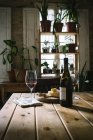 Bottiglia aperta e bicchieri con vino rosso posizionati vicino al formaggio sul tavolo di legno in ristorante rustico con piante verdi in vaso sulla finestra — Foto stock