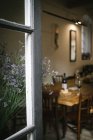 Fragment of interior of rustic restaurant with wooden table served with wine and cheese seen from open window with flowers — Stock Photo