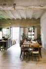 Большой деревянный стол и стулья в деревенском баре в стиле ретро с потрепанным потолком и зелеными растениями на окне — стоковое фото