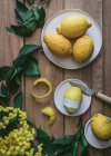 Top view of peeled and fresh lemons on plates on wooden table with green leaves and yellow flowers — Stock Photo