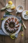 Draufsicht von oben leckerer frischer veganer Kuchen mit Zitrone und Kokosnuss überzogen mit Glasur auf Holztisch mit Zutaten — Stockfoto