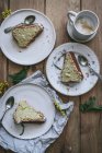 Вид зверху на скибочки свіжого веганського лимона та кокосового торта на тарілках з ложками та чашкою кави — стокове фото