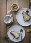 Вид зверху на скибочки свіжого веганського лимона та кокосового торта на тарілках з ложками та чашкою кави — стокове фото