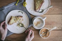 Draufsicht auf gesichtslose Dame mit Tasse Kaffee am Holztisch mit leckeren Stücken veganer Zitronen- und Kokosnusstorte beim Frühstück — Stockfoto