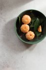 Вид зверху на зелену керамічну миску зі свіжими очищеними мандаринами, розміщеними на білому столі біля неочищених фруктів з зеленим листям — стокове фото