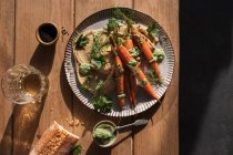 Vista superior de fatias de pão fresco espalhadas com hummus na placa com cenouras laranja assadas decoradas com molho verde na mesa de madeira — Fotografia de Stock