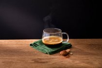 Скляна чашка ароматної гарячої чорної кави на зеленій серветці, розміщеній з ложкою меленої кориці на дерев'яному столі з чорним фоном — стокове фото