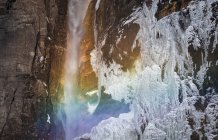 Amazing scenery with rainbow at small waterfall falling from sheer cliff and frozen rocky wall in Canadian countryside — Stock Photo